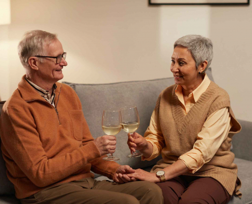 Senioren auf einer Couch prosten sich mit einem Weinglas zu.